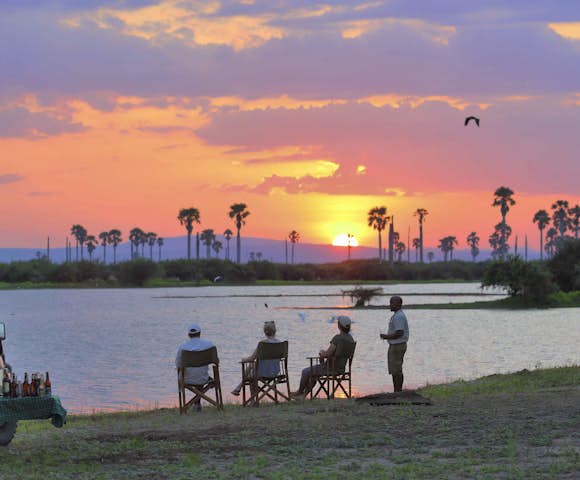 People sitting in front of lake with sunset, Selous Game Reserve