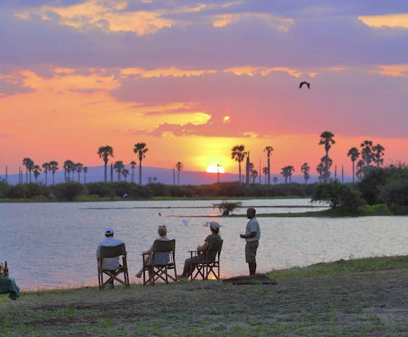 People sitting in front of lake with sunset, Selous Game Reserve